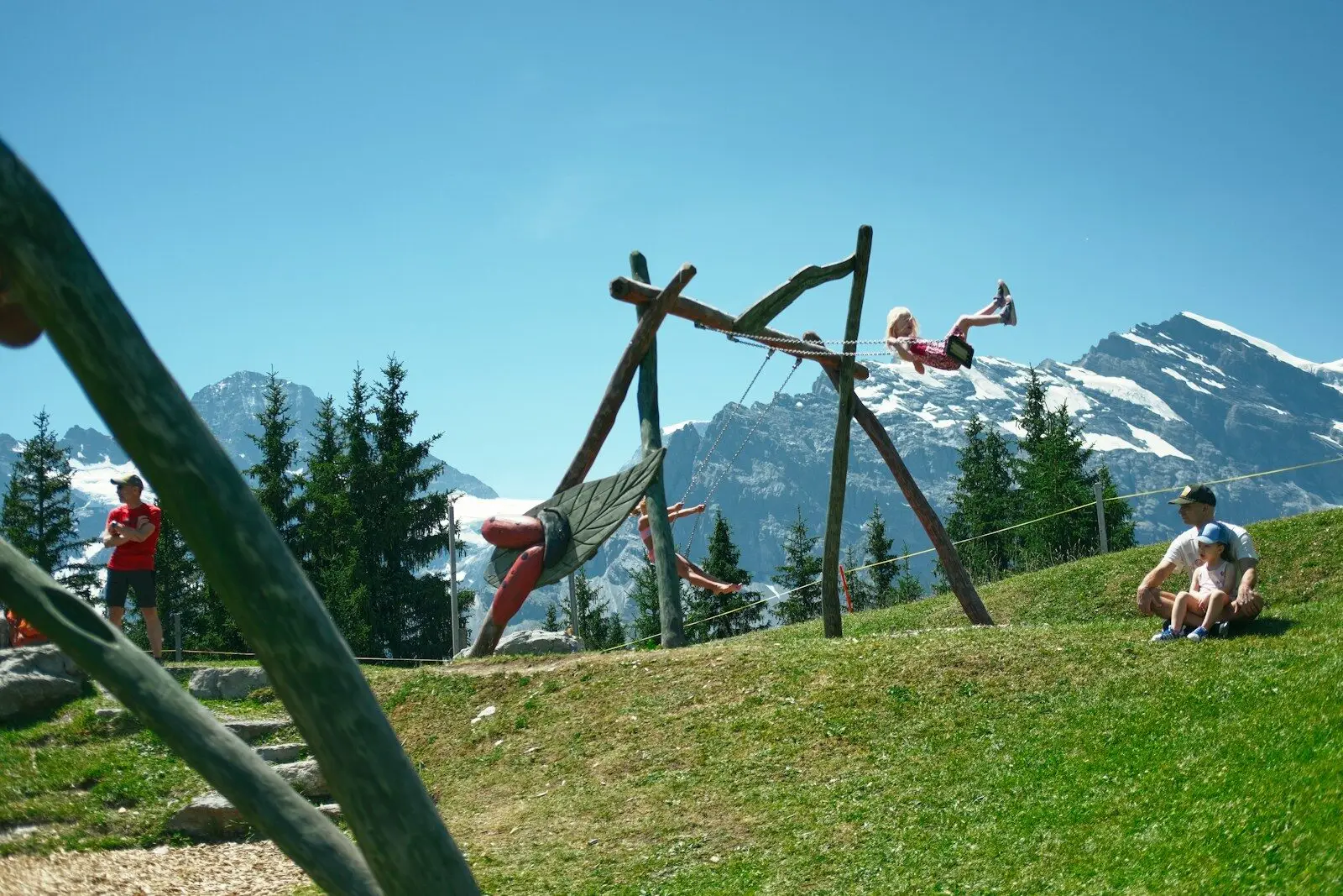 Children playing on swings in a mountain playground.